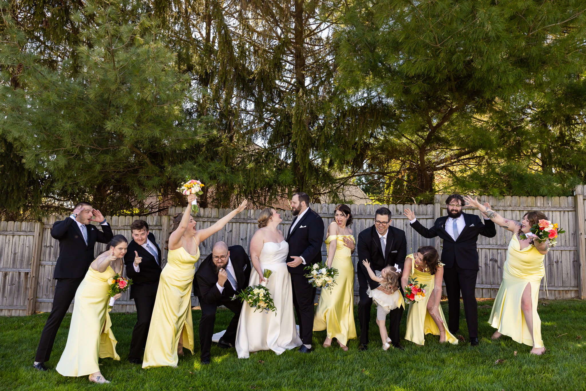 Bride and Groom look at each other as their wedding party strike a pose around them. The groomsmen are wearing black suits and the bridesmaids are in yellow dresses