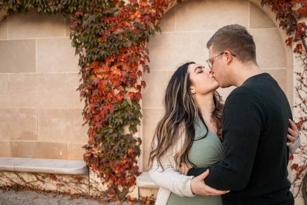 Wrapped in autumn’s warm hues, a couple shares a kiss against an ivy-covered stone wall at Longwood Gardens. The rich colors and romantic textures of the season create an unforgettable engagement photo in this iconic garden