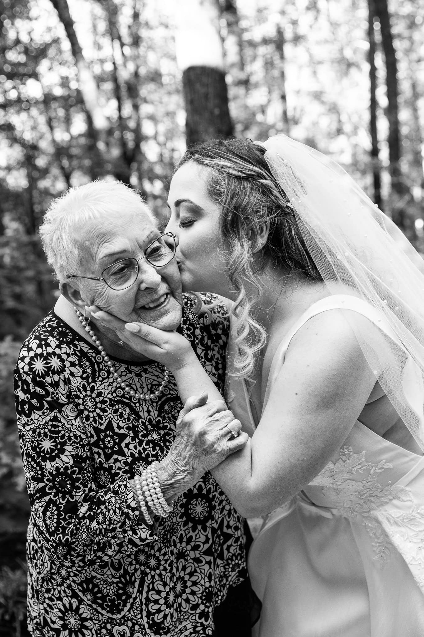A bride kisses her elderly grandmother’s cheek in a tender, emotional black-and-white portrait. This heartfelt family wedding photo is a tribute to the wisdom, love, and legacy that older generations bring to a wedding day.