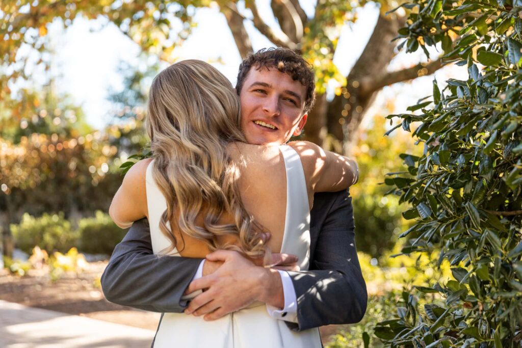Ellie and Logan embrace after their first look, surrounded by fall foliage and the natural beauty of The Gardens at The Venue Chattanooga. Their classic black and white wedding colors contrast beautifully with the golden autumn tones.