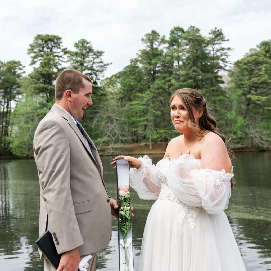 The groom stands across from the bride, who clutches a slim black box holding a single pink rose and delicate baby’s breath—the moment she reveals their baby’s gender. Her expression is full of emotion, her lips trembling and hand resting on her chest. This deeply personal reveal was one of the most unforgettable parts of their Medford, NJ wedding day.