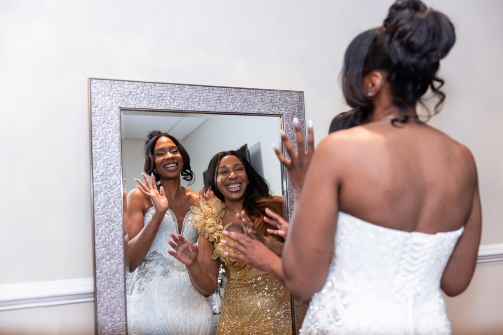 Zer stands in her beaded gown, facing a mirror, laughing alongside her mom, who is dressed in a sparkling gold gown. Both are glowing, caught in a joyful getting-ready moment before the Merion wedding ceremony begins.