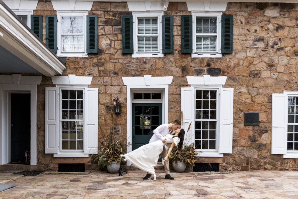The groom-to-be dips the bride-to-be into a joyful kiss in front of the iconic stone façade of Elizabeth Furnace, setting the tone for their upcoming Elizabeth Furnace wedding.