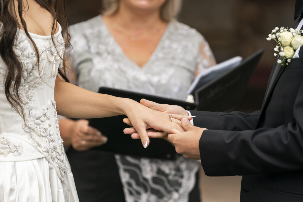 Noah gently slides a wedding ring onto Alyssa’s finger as she holds out her hand. Both of their hands are framed tightly in the image, with blurred greenery and florals in the background. This Lancaster wedding photo highlights a quiet, tender exchange in their vow ceremony.
