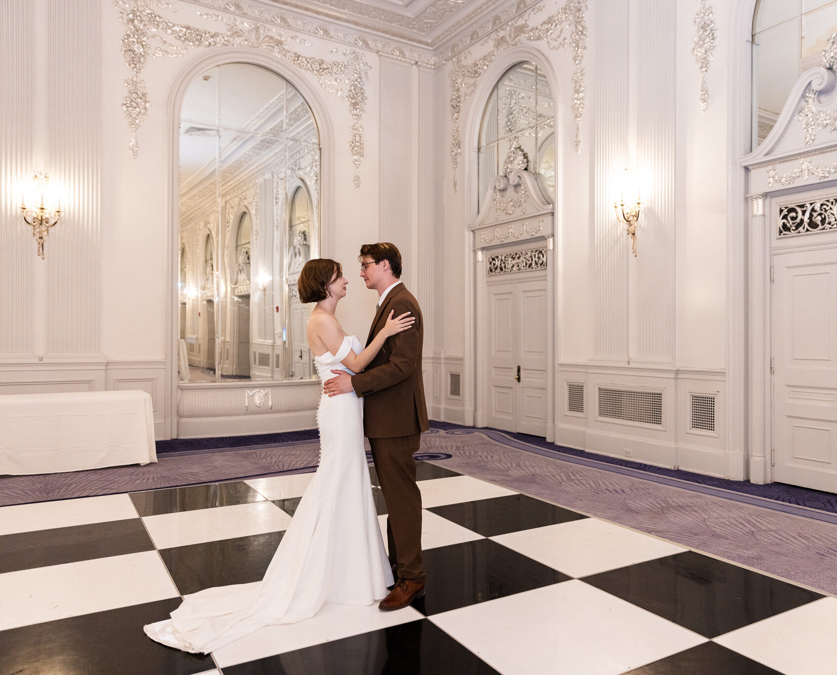 Bride and groom share a quiet first dance on the black-and-white checkered floor of the Chestnut Room during their Read House Wedding Reception, surrounded by ornate white walls and grand mirrors.