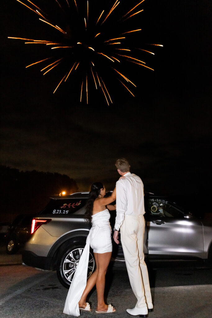 At night, the newlyweds stand side by side watching a burst of fireworks in the sky. Behind them, their getaway car is decorated with wedding-day details, closing the celebration in the spirited style often seen at outdoor wedding venues in Chattanooga.