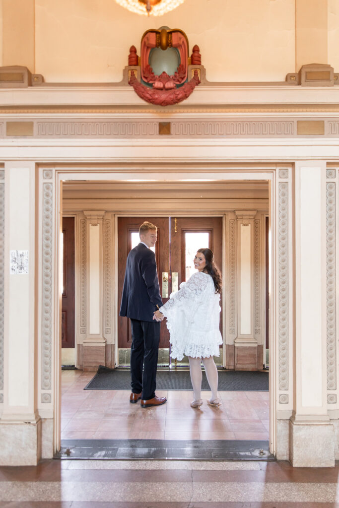 Inside the Chattanooga Choo Choo, the couple holds hands and looks back toward the camera, framed by ornate cream-colored archways and vintage wooden doors, adding a timeless touch to their engagement portraits.