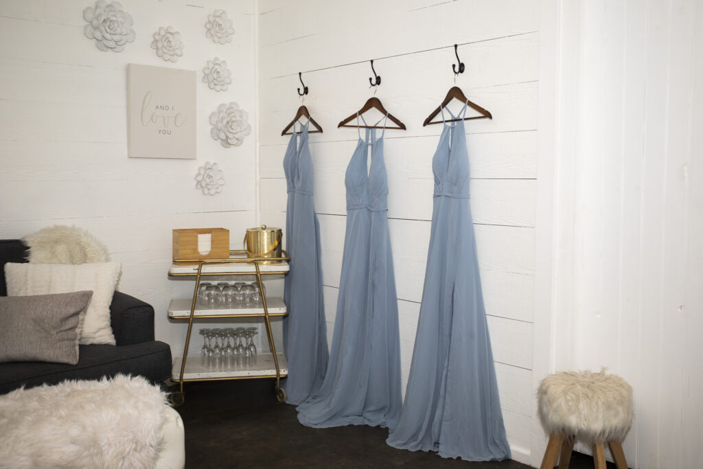 Bridesmaid dresses hanging on wooden hangers during wedding dress planning in a bridal suite with white walls and cozy décor.