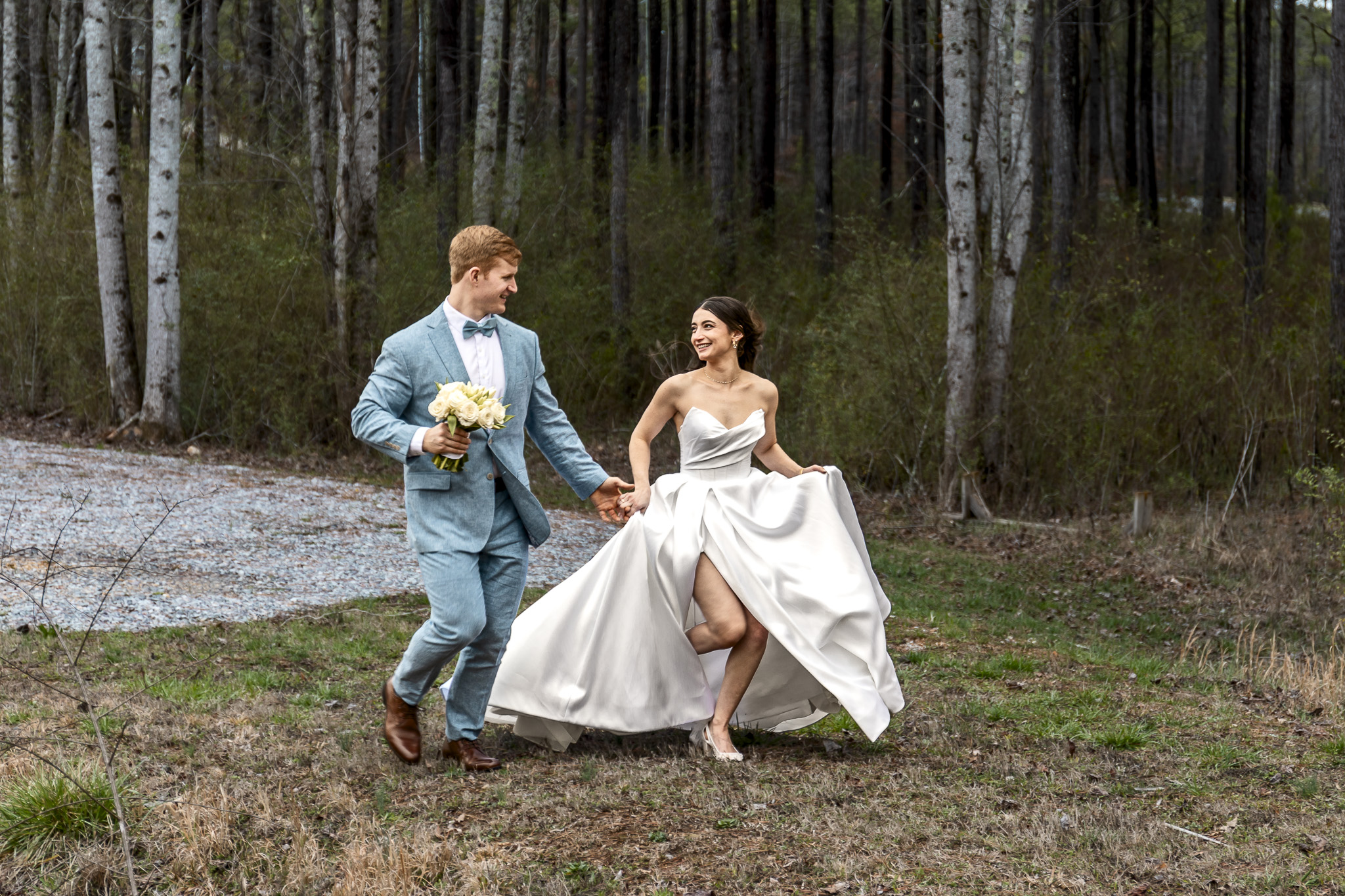 Bride lifting her dress while walking with the groom through a wooded path, showcasing comfort and mobility from wedding dress planning.