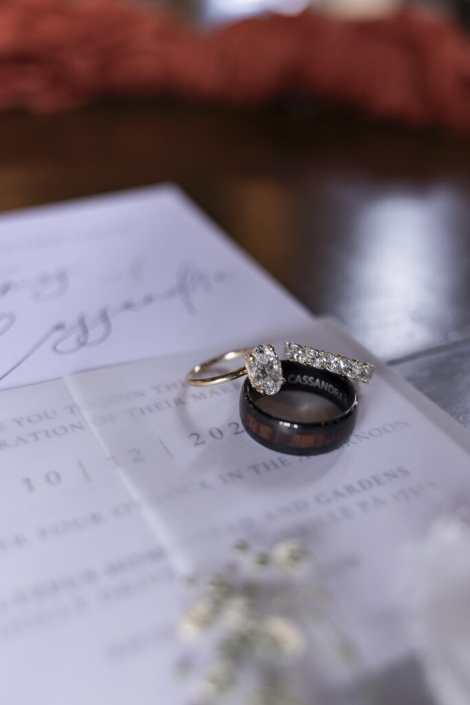 A close-up of the couple’s wedding rings rests on their invitation suite, the engraved bands and sparkling diamonds catching soft morning light during their Stoltzfus Homestead Wedding preparation.