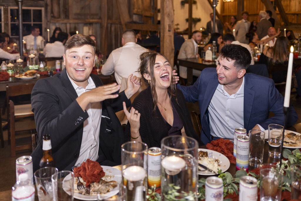 Friends gathered at long wooden tables share laughter and stories late into the night, the barn at Stoltzfus Homestead Wedding glowing with candlelight and the energy of celebration.
