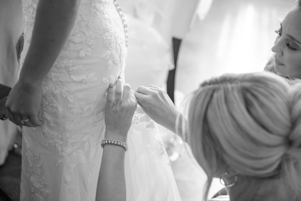 Candid black-and-white moment of bridesmaids bustling the bride’s dress, capturing the quick transition into the wedding reception