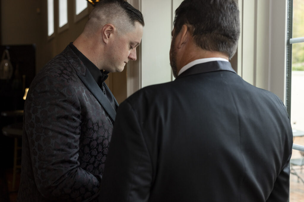 The groom shares a quiet, emotional moment with the father of the bride inside the Pyn Ryn Estate. Standing near the window, he takes a breath before walking out to begin the ceremony, reflecting the anticipation of the Pyn Ryn wedding day ahead.