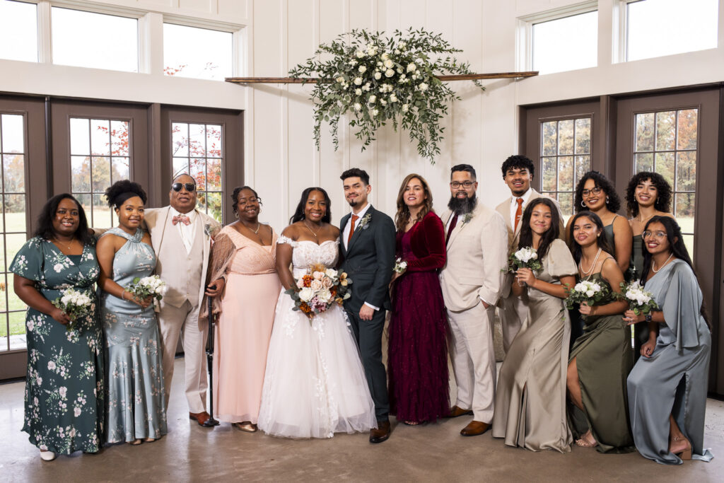 wedding family photo featuring both the bride and grooms immediate family at an indoor location with florals hanging above them and doors on either side