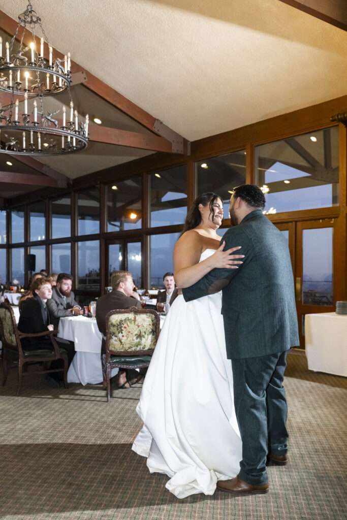 The couple shares their first dance inside a reception room at a Lookout Mountain wedding venue, surrounded by guests seated at round tables beneath chandeliers and wood-beamed ceilings.