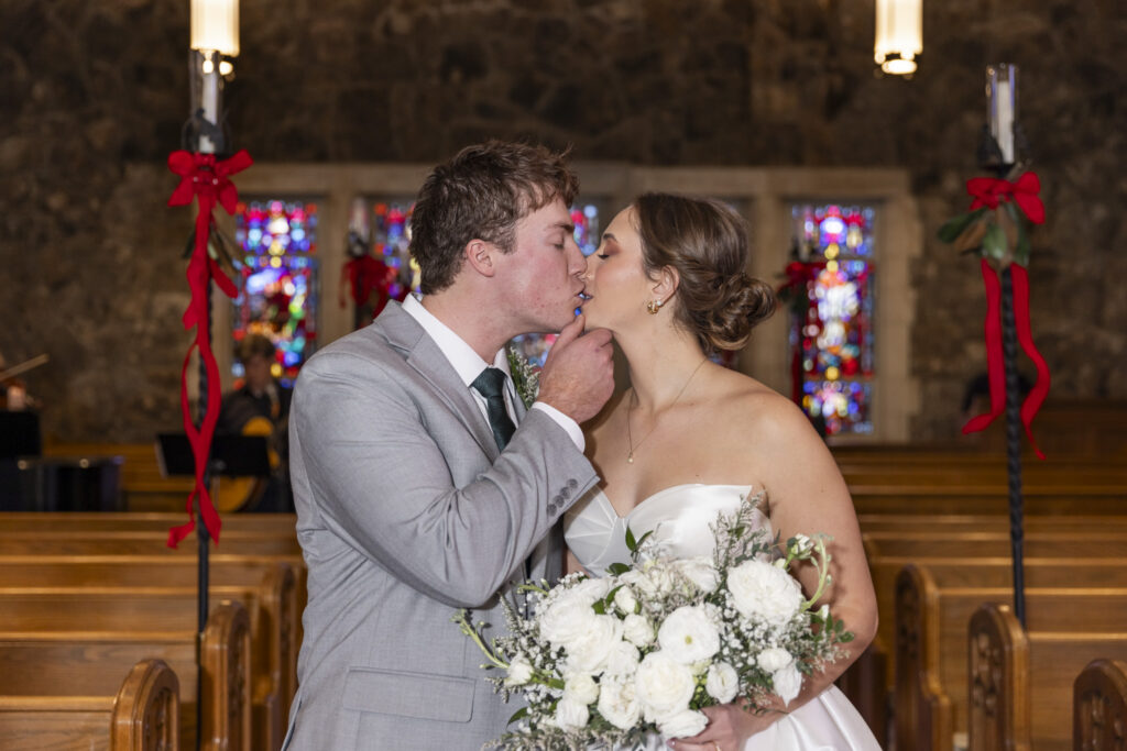 The groom gently cups the bride’s chin as they share a kiss in the aisle, her bouquet held close and pews framing the moment in this intimate Chattanooga Church Wedding.