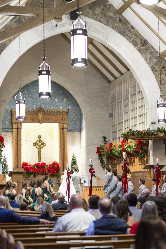 From the congregation’s perspective, the couple stands at the altar facing one another beneath arched stone architecture and soft candlelight, surrounded by guests during their Chattanooga Church Wedding ceremony.