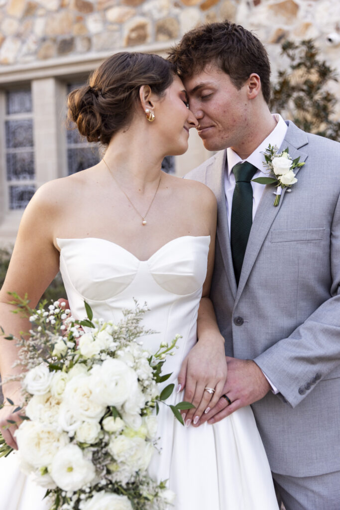 A close, intimate portrait of the couple with their foreheads gently touching, eyes closed as they breathe into the moment. The bride’s hair is pulled into a low bun, pearl earrings visible, while the groom’s boutonniere rests against his light suit jacket. The stone exterior of the church blurs behind them, centering this tender pause during their Lookout Mountain Presbyterian Wedding.