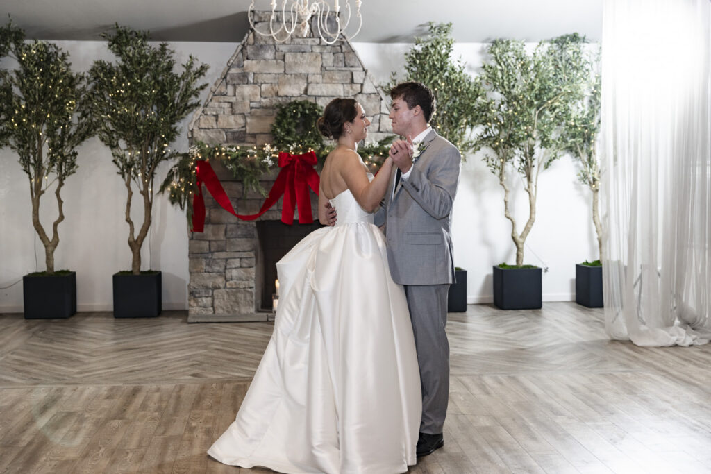 The bride and groom share their first dance alone on the floor, bodies turned toward each other as they hold hands and sway gently. Potted trees and a stone fireplace create a balanced backdrop, while the open floor emphasizes their connection. The quiet intimacy of this first dance anchors The Venue Chattanooga wedding evening.