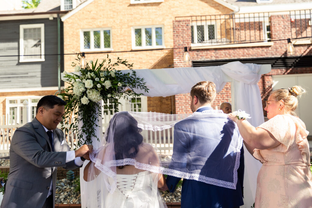 Family members carefully place a ceremonial veil over the bride and groom during a traditional Filipino wedding ritual incorporated into their Princeton wedding venue ceremony.