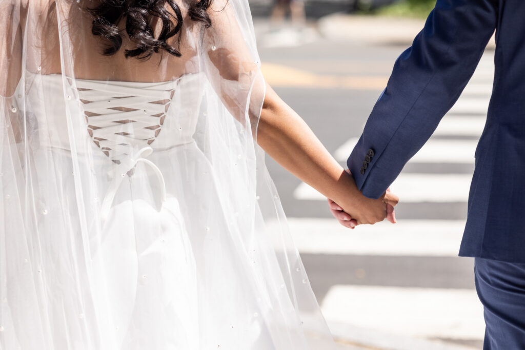 Bride and groom hold hands while walking through downtown Princeton, the bride’s pearl-detailed veil trailing softly behind her during portraits near their Princeton wedding venue.