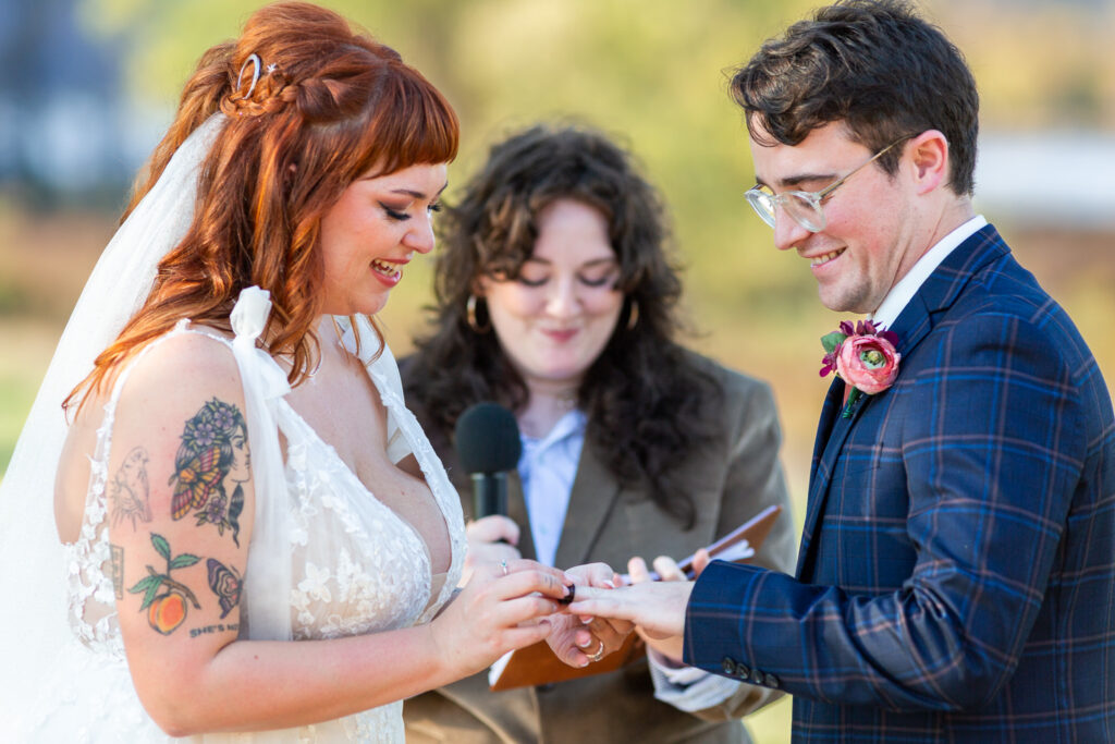 Couple exchanges wedding rings during an outdoor ceremony led by a close friend serving as officiant, creating a meaningful and personal experience as they make their marriage official.