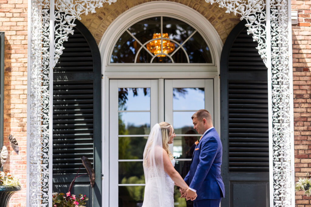 The bride and groom share a quiet first look beneath the decorative iron canopy outside the manor house, a timeless moment from their Drumore Estates wedding day.