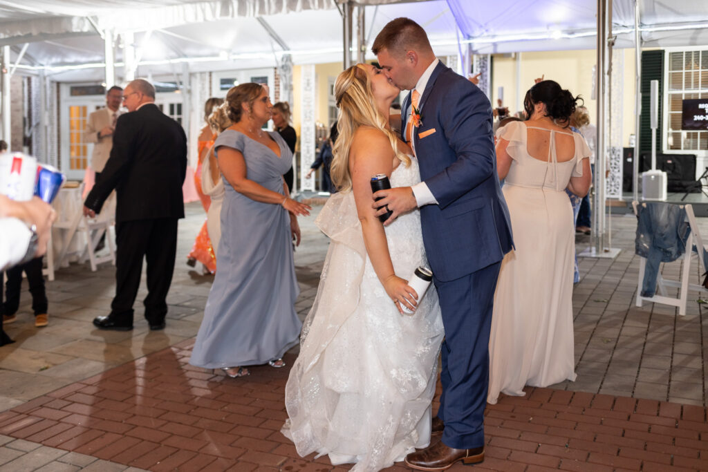 Bride and groom share a kiss on the dance floor during their Lancaster Wedding reception. Guests mingle beneath a clear tent while the couple pauses for a quiet moment together amid the celebration.