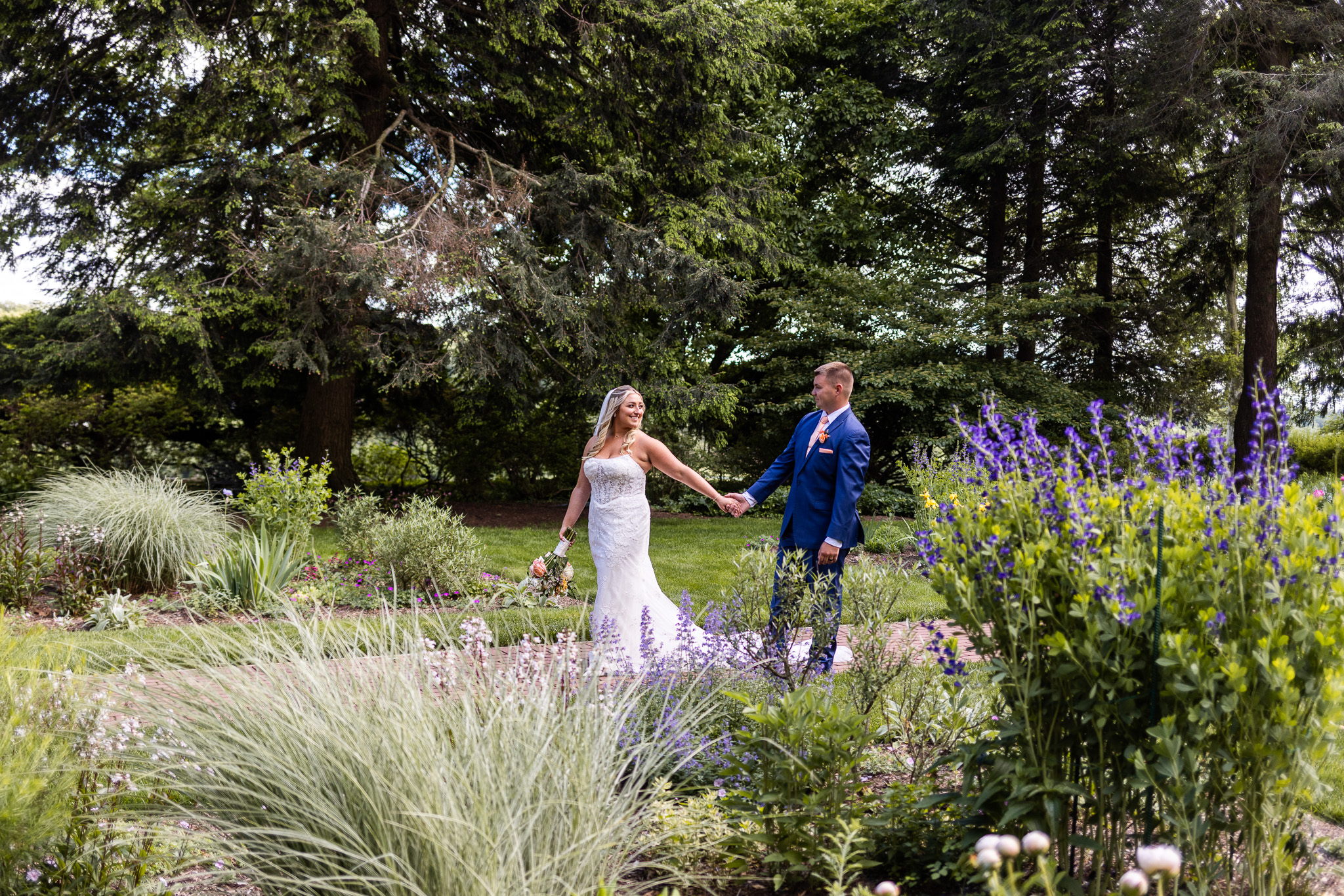 The newlyweds stroll hand in hand through the estate gardens, surrounded by colorful flowers and lush greenery during their Drumore Estates wedding portraits.