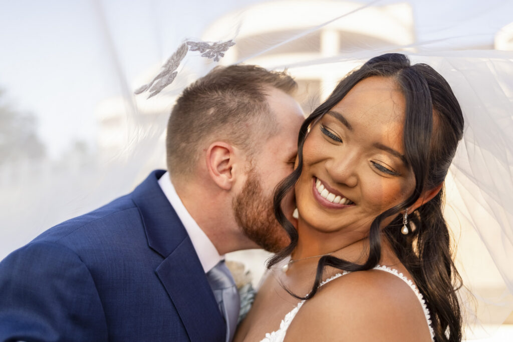Bride and groom kiss beneath her flowing veil in a close-up portrait filled with warm evening light during their wedding at The Mansion on Main Street.