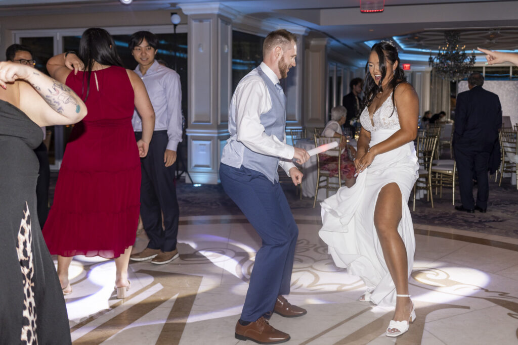 Bride and groom dance together on the reception floor, laughing as colorful DJ lighting fills the ballroom during their south jersey wedding celebration.