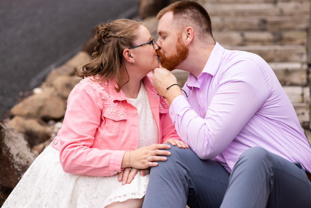 Newly married couple shares a close kiss during romantic couples portraits, seated together beside rustic wooden steps at their Pennsylvania wedding venue.
