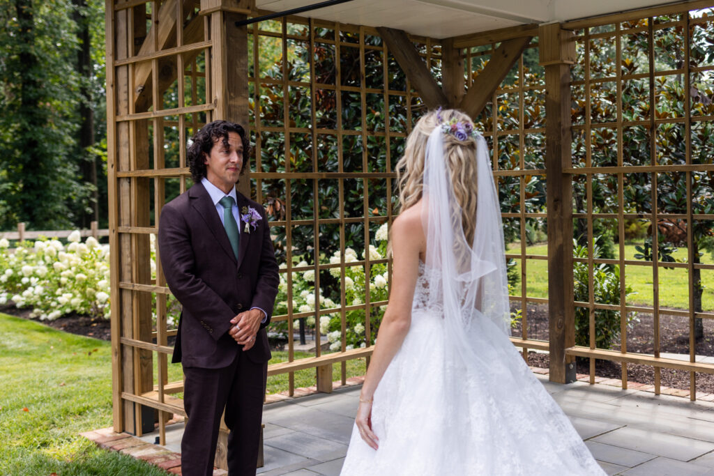 A couple sees each other during their first look beneath the wooden garden pergola at their Founders Grove wedding, surrounded by white hydrangeas and greenery.