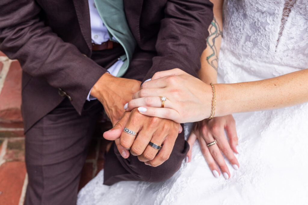 A close-up from a South Jersey wedding shows the newlyweds resting their hands together, displaying their wedding bands and the bride’s square-cut engagement ring.