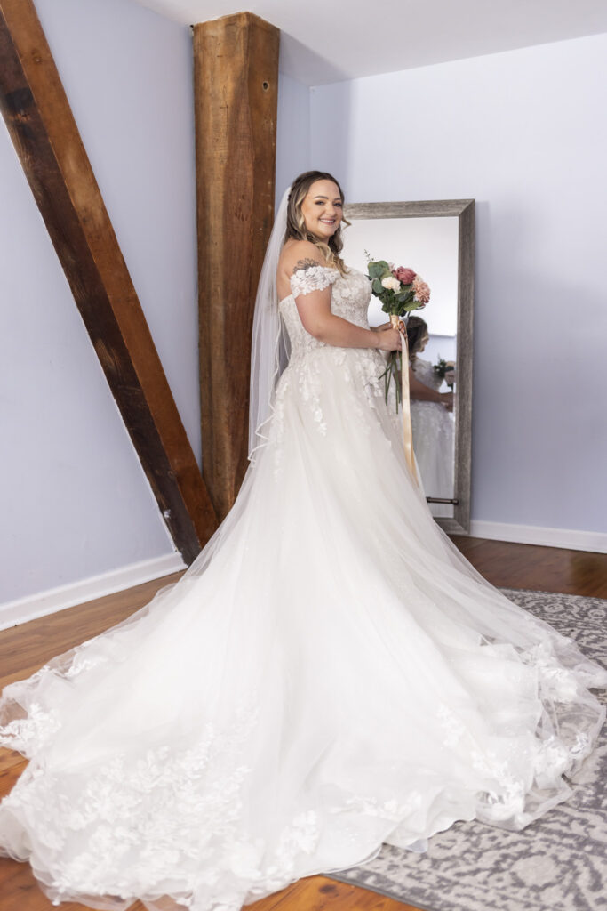 Bride poses indoors in her lace wedding gown and long veil, holding a pink and white bouquet before her Tyler Arboretum wedding.