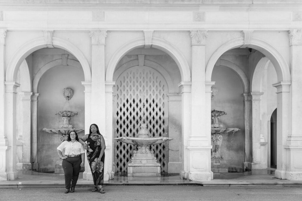 Black-and-white portrait from a Longwood Gardens proposal, with the engaged couple standing together beneath grand stone arches and beside ornamental wall fountains in a formal architectural garden.