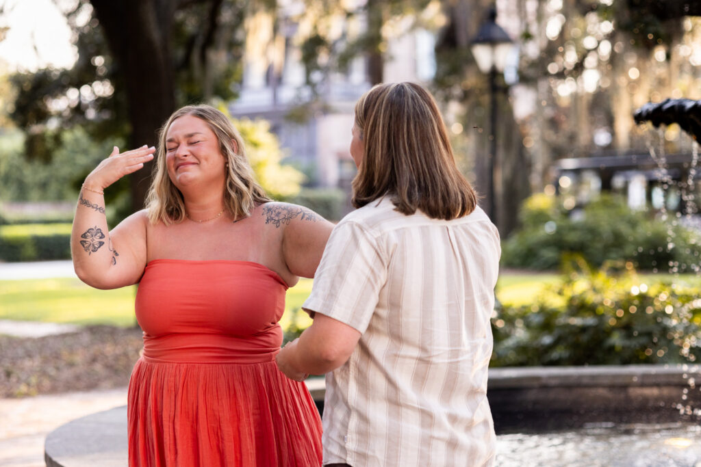 Emotion takes over moments after an LGBTQ proposal in Savannah as the newly engaged woman fans at tears on her face while holding her partner’s hand beside the fountain in Lafayette Square.