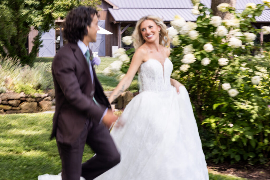 A couple runs hand in hand through the gardens during their Founders Grove wedding, photographed with intentional motion blur beside blooming white hydrangeas.